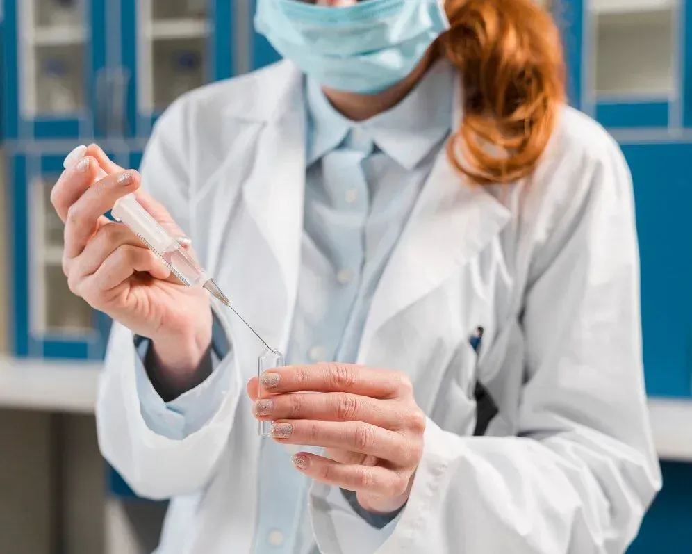 A female doctor is wearing a mask and holding a syringe.