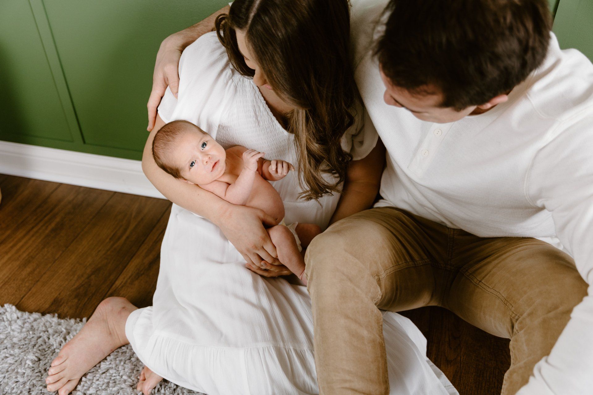 Mom and dad sit on the ground and hold newborn baby boy