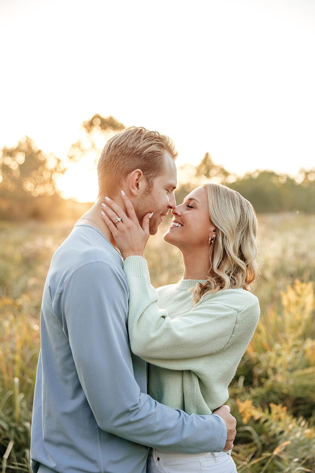 Couple embracing outdoors, golden light, smiling, near touch, fields.