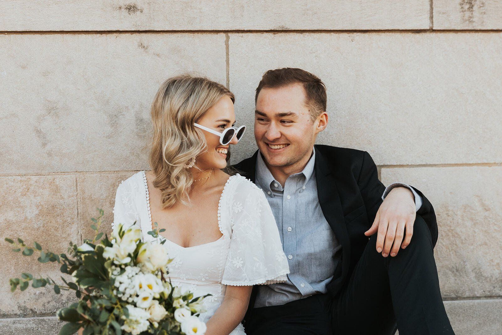 Engaged couple look at eachother while woman holds a bouquet