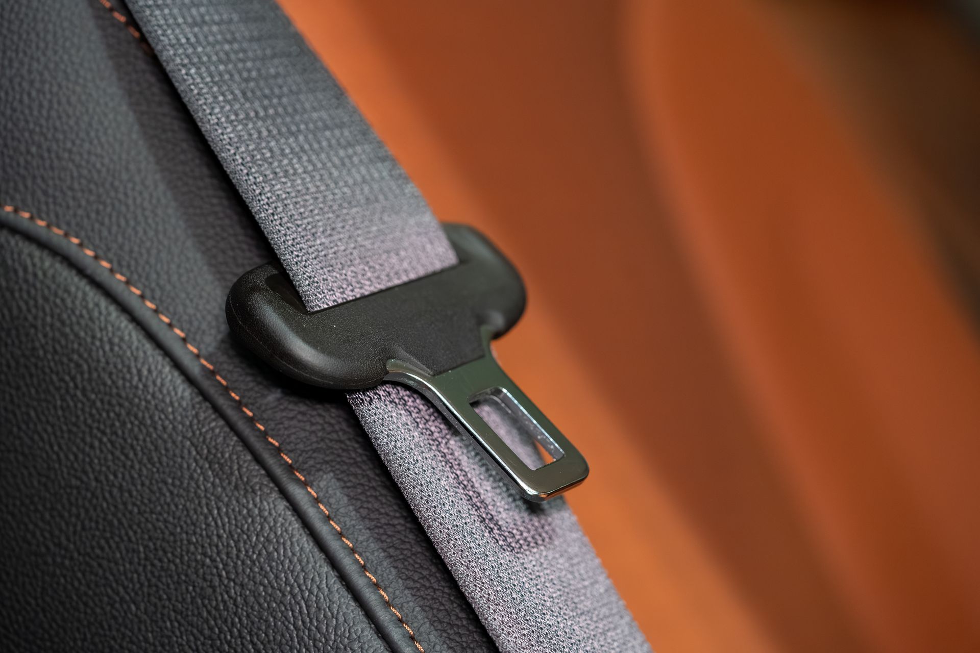 Close-up of a gray seatbelt latch on a black car seat with orange upholstery background