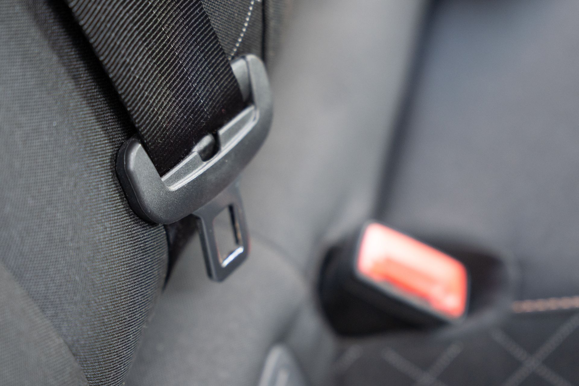 Close-up of a black car seatbelt buckle and strap on a dark fabric seat, with a red latch in the background Close-up of a black car seatbelt buckle and strap on a dark fabric seat, with a red latch in the background