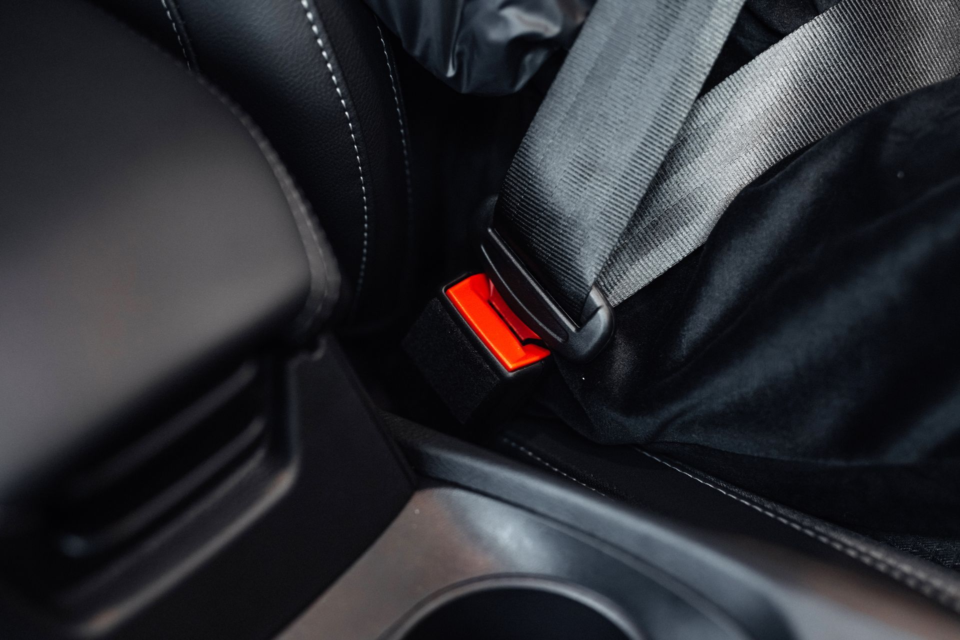 Close-up of a car seatbelt buckle with a red release button beside a black seat and cup holder