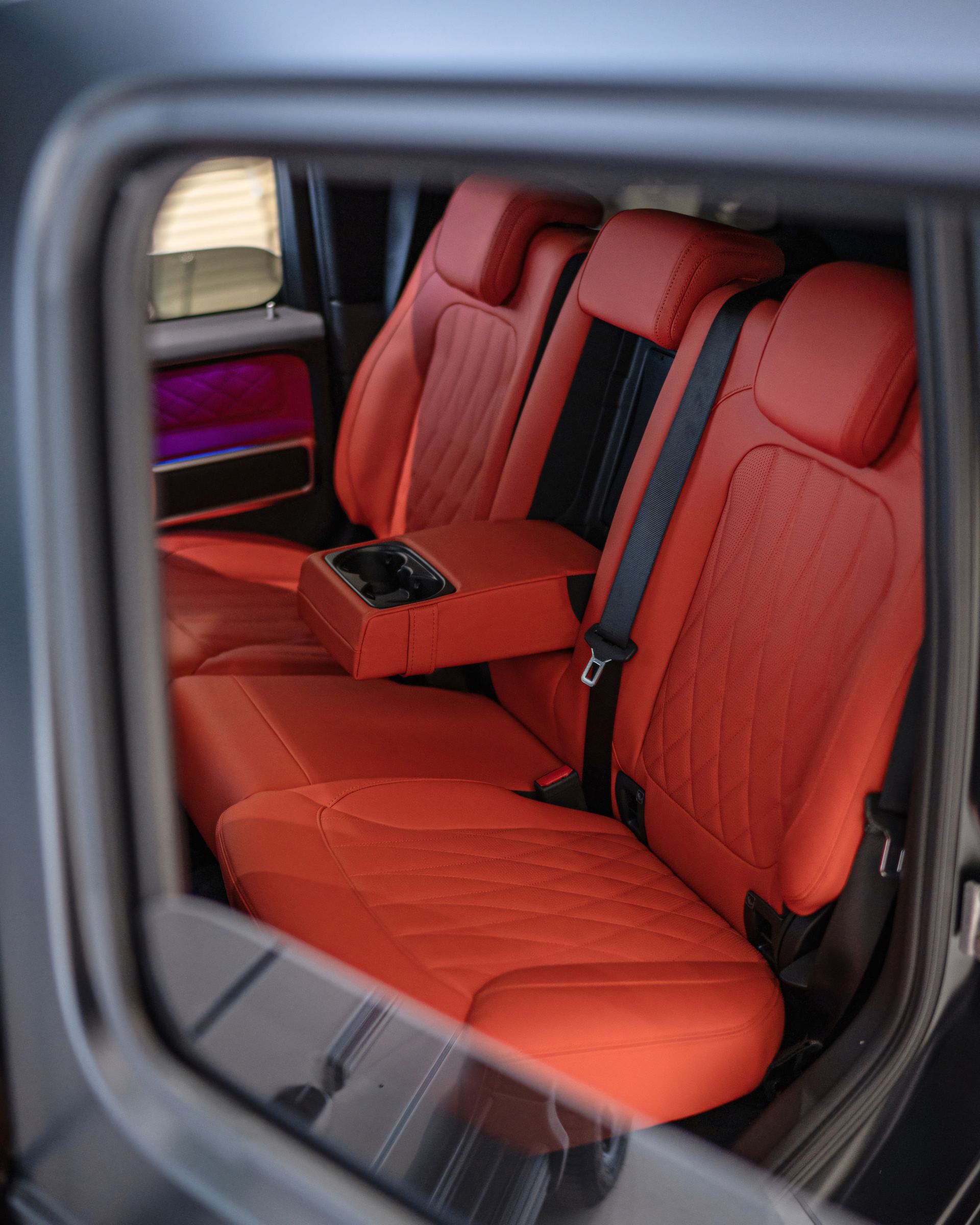 Red leather car back seat with center armrest and seatbelts, viewed through an open door Red leather car back seat with center armrest and seatbelts, viewed through an open door