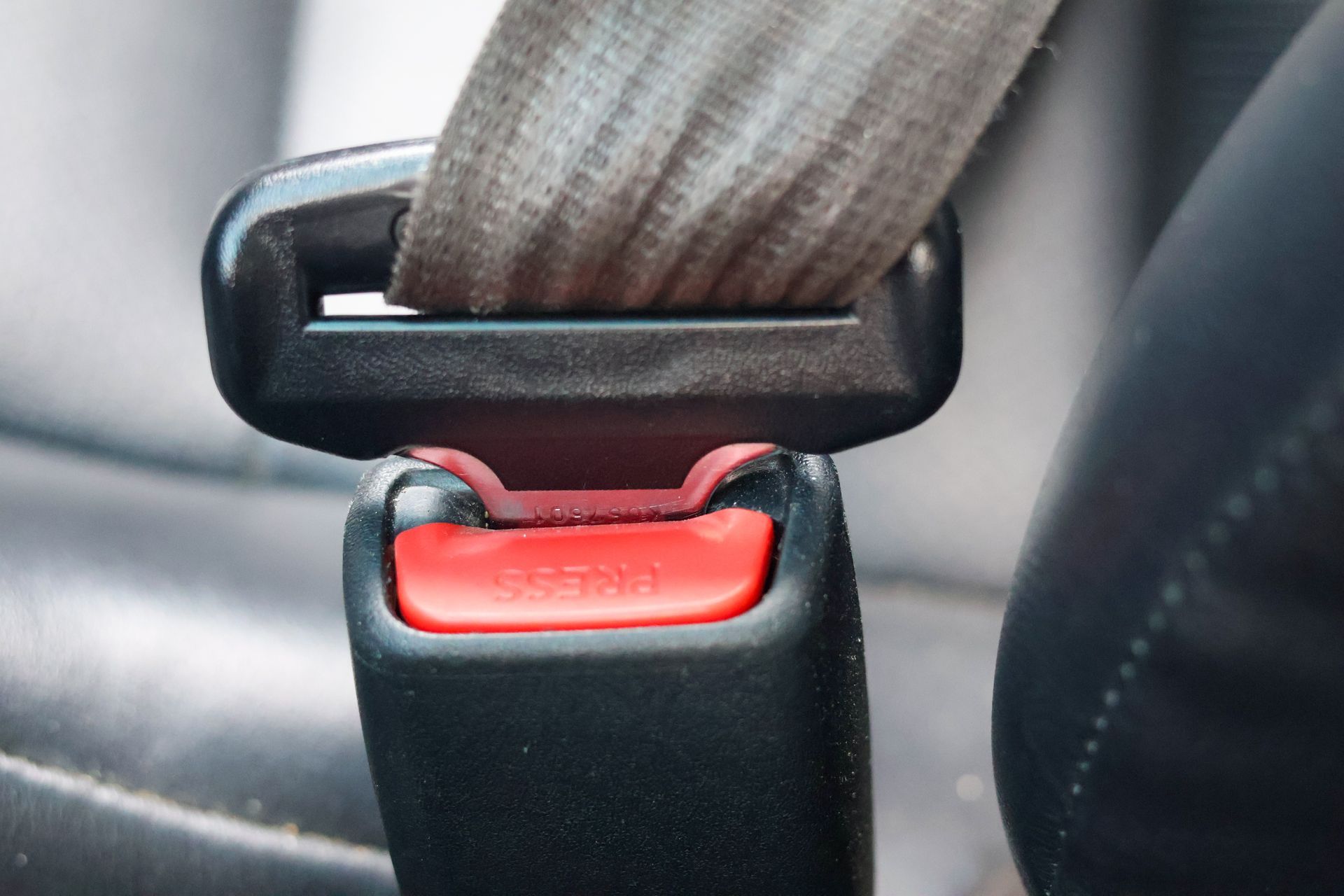 Close-up of a car seat belt buckle with a red release button and gray strap