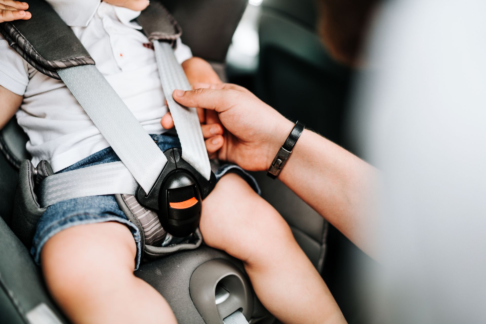 Infant secured in a car seat while an adult fastens the harness strap