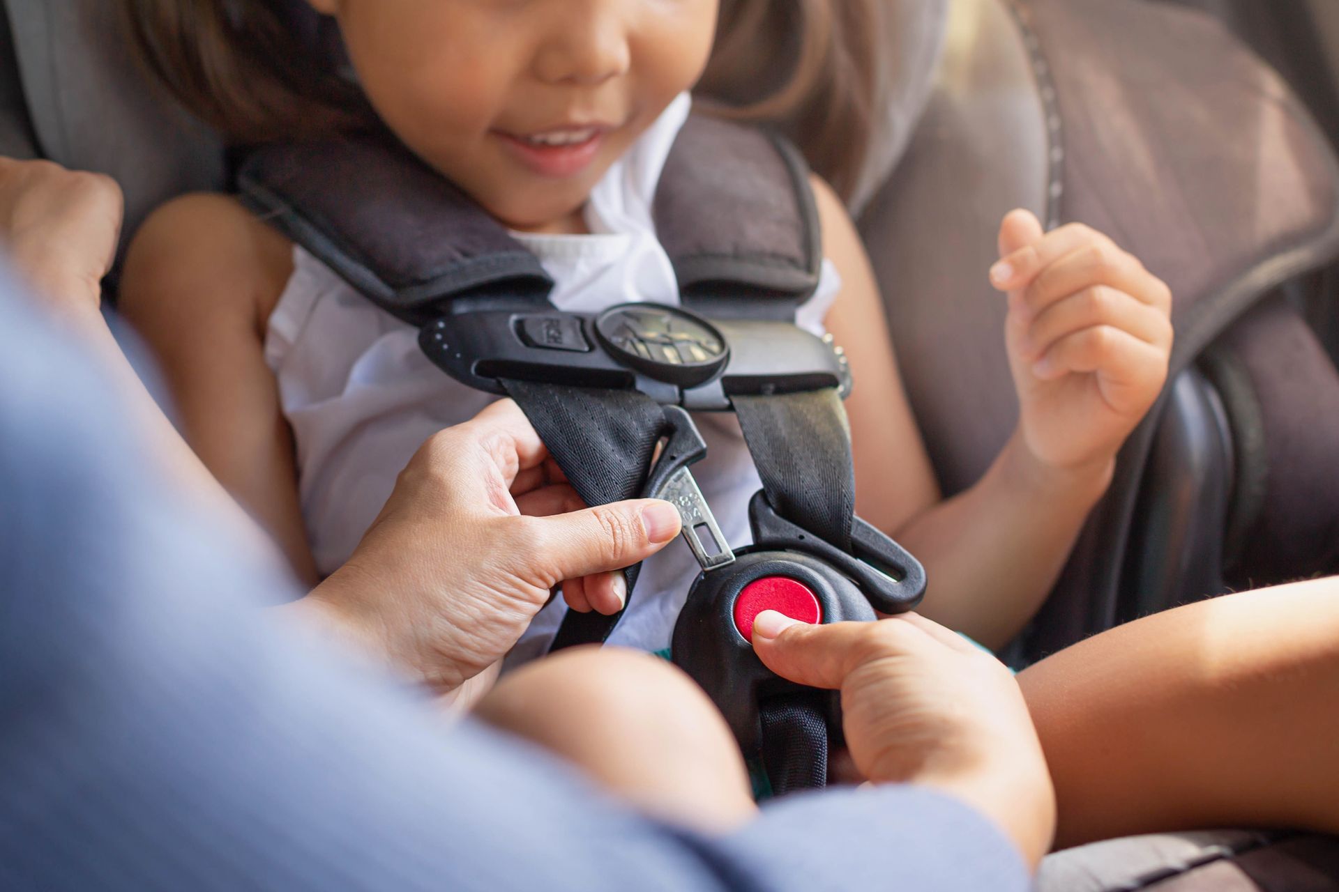 Adult fastening a child's car seat harness with a red buckle in a vehicle Adult fastening a child's car seat harness with a red buckle in a vehicle