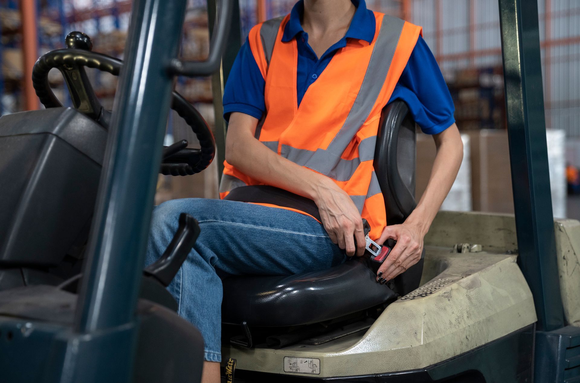 Worker in orange safety vest seated in a forklift cab, holding the control lever.