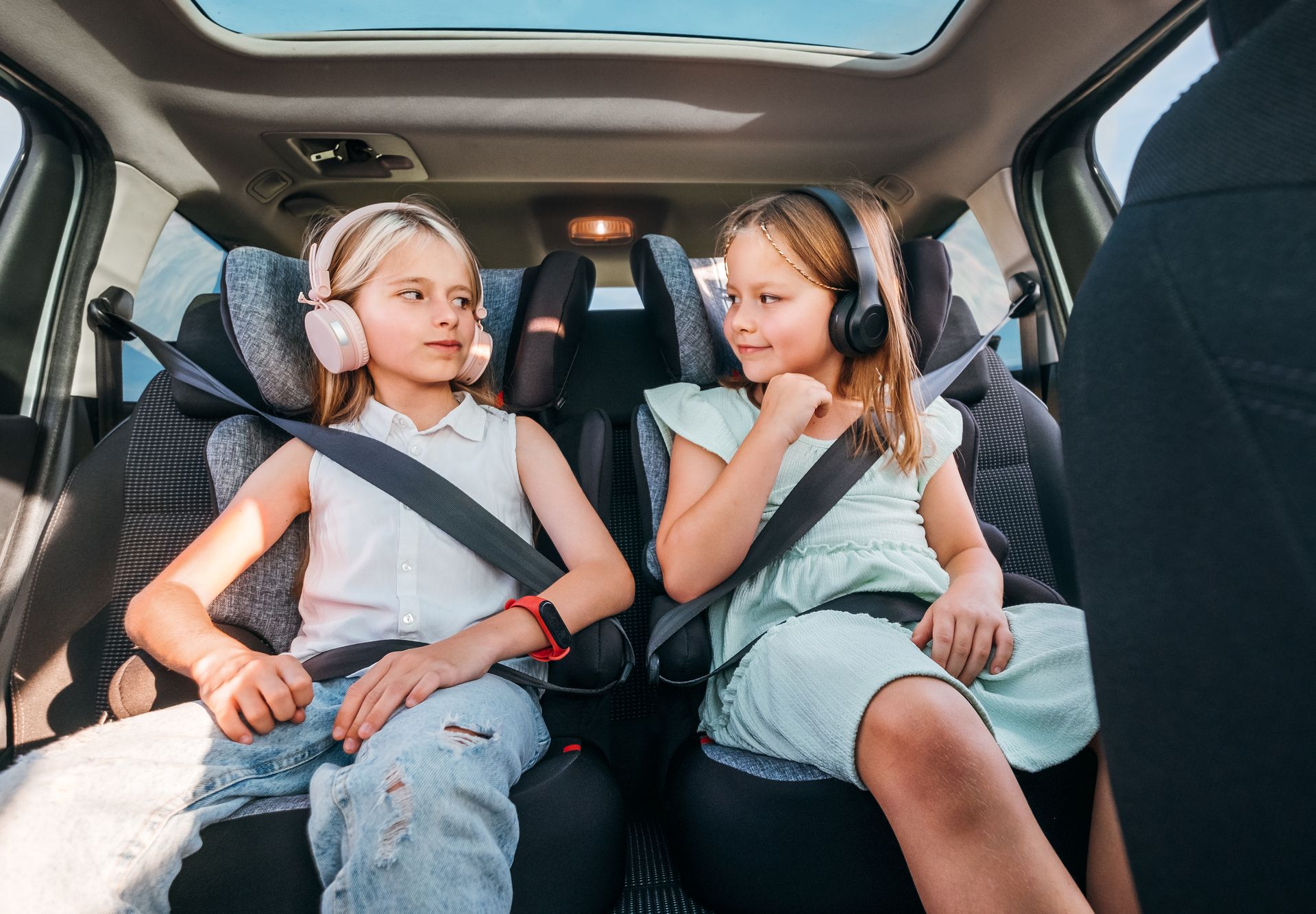 Two children wearing seat belts sit in the back seat of a car, looking at each other and smiling. Two children wearing seat belts sit in the back seat of a car, looking at each other and smiling.