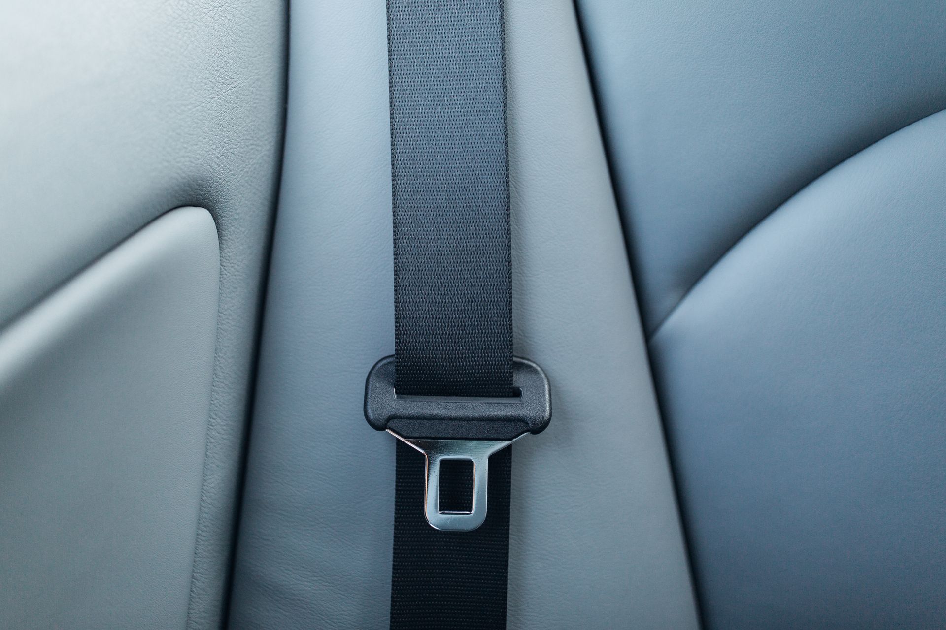 Close-up of a gray car seatbelt with buckle against a light gray seat.