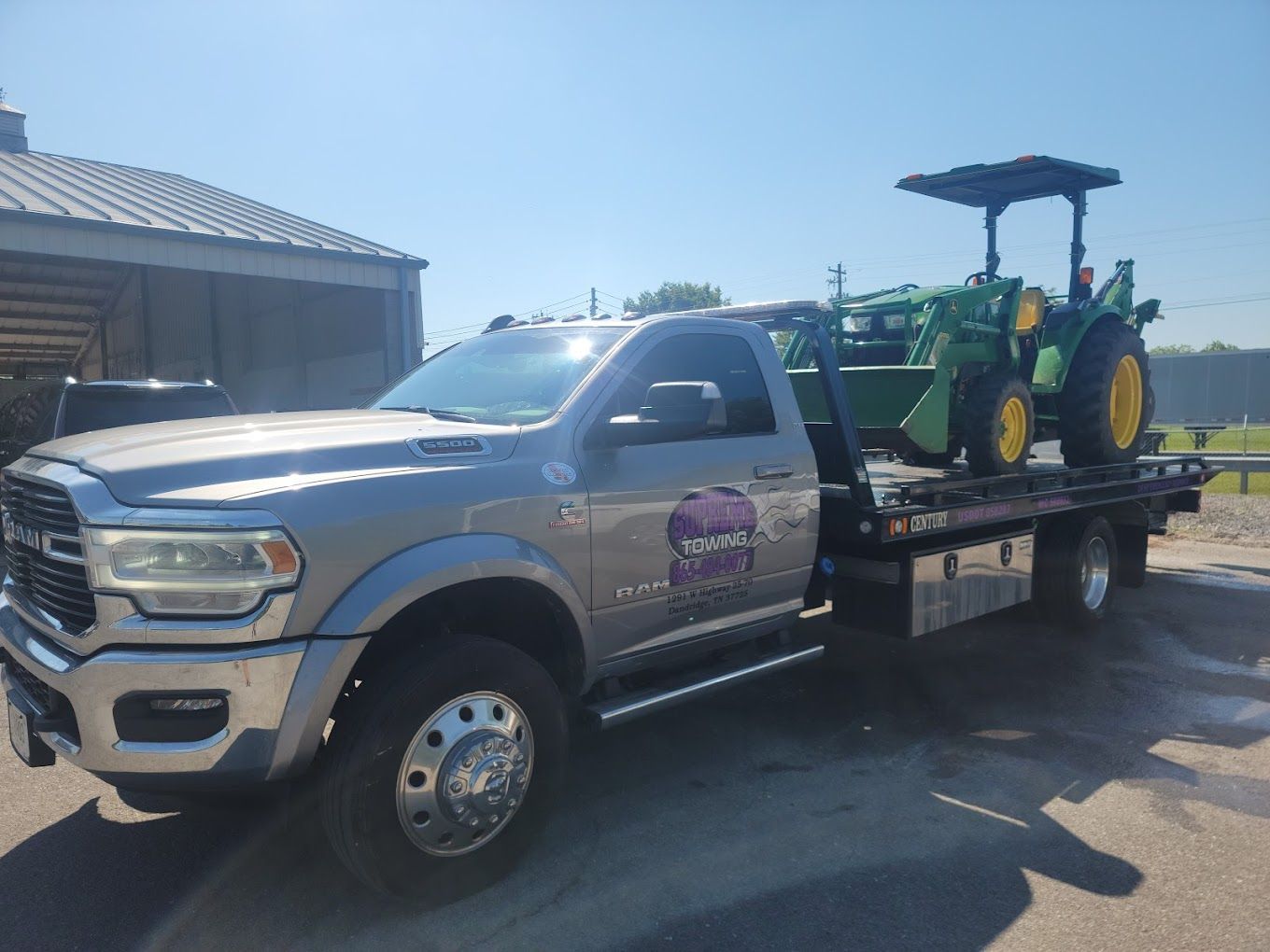 A tow truck is carrying a green john deere tractor.