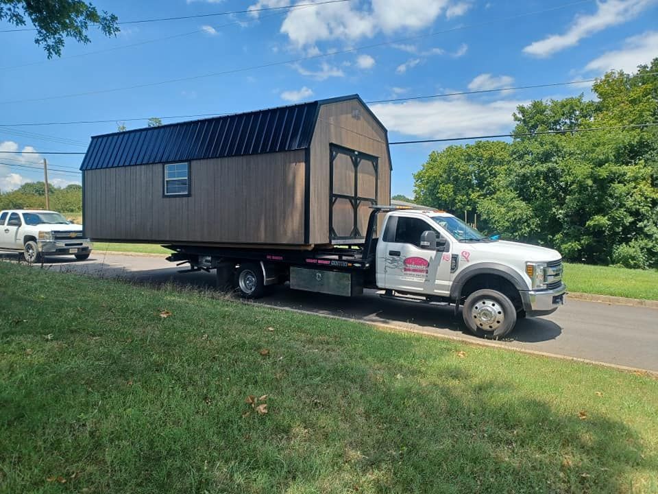 A tow truck is towing a shed down a road.