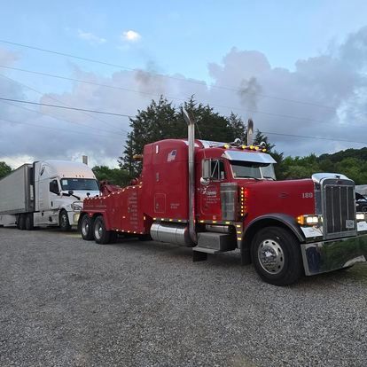 A red tow truck is parked next to a white semi truck