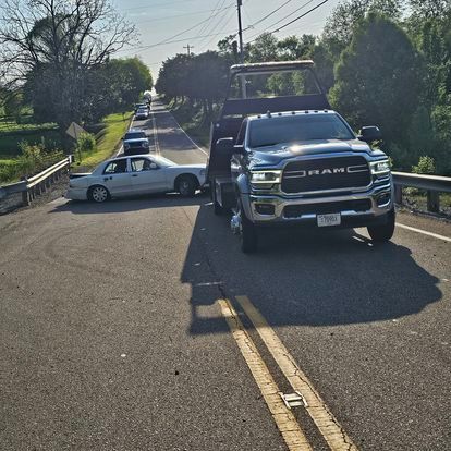 A tow truck is towing a white car on the side of the road.