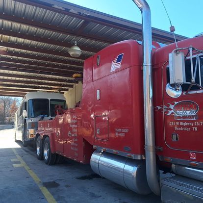 Two red tow trucks are parked under a covered area