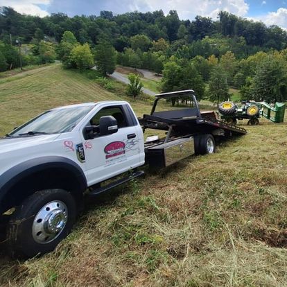 A tow truck is towing a tractor in a field.