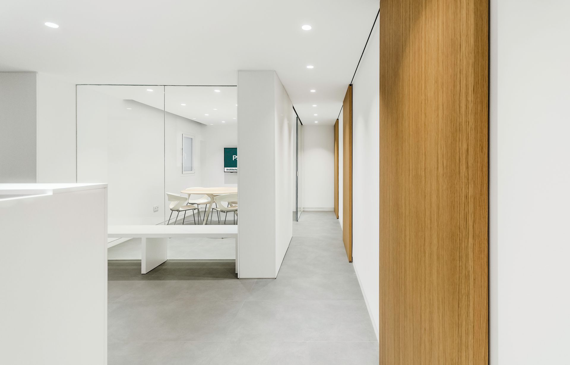 Pasillo luminoso y moderno con paredes blancas, suelo gris y un dormitorio visible a través de una puerta abierta.