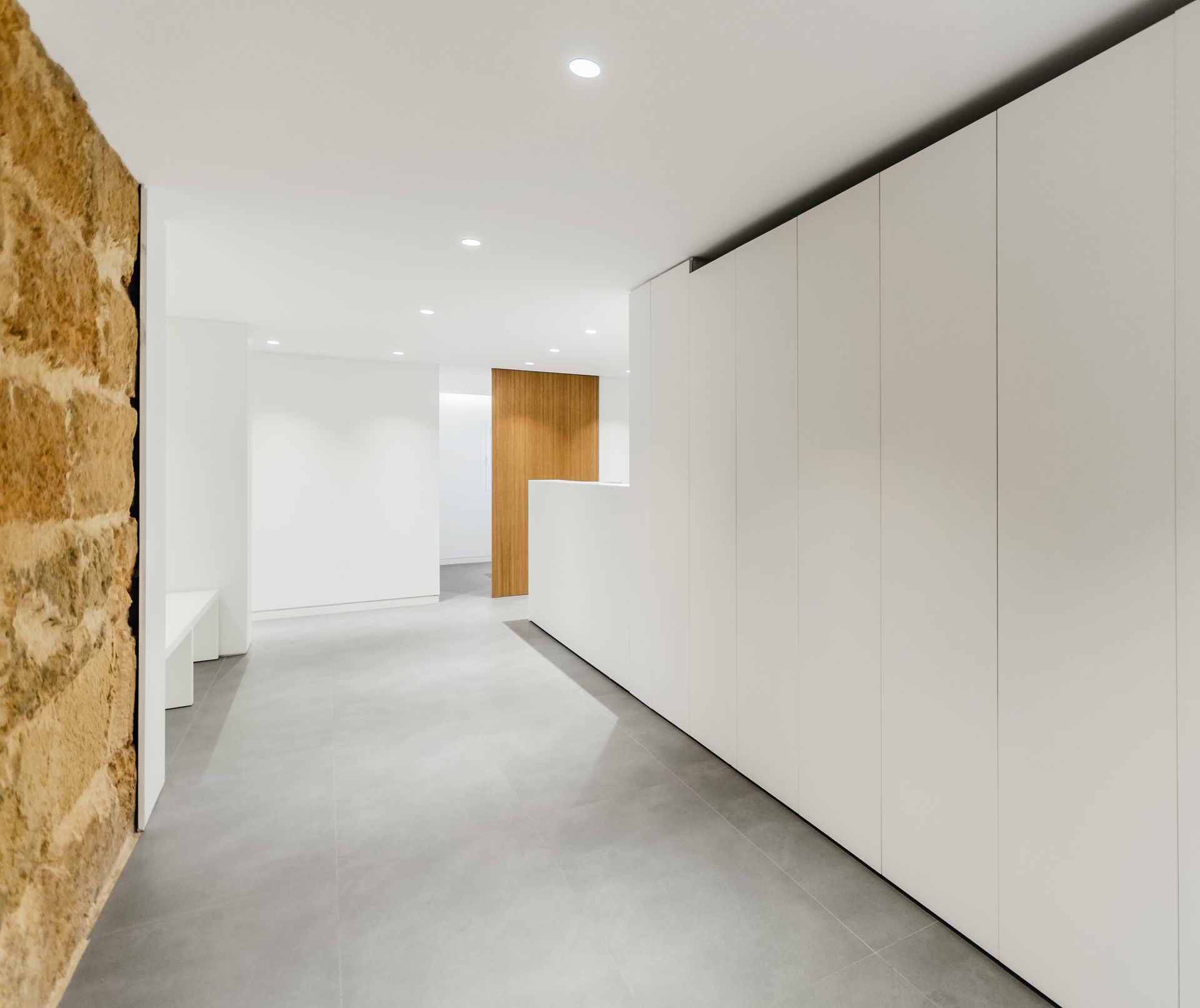 Pasillo moderno minimalista con paredes blancas, suelo gris y pared decorativa de madera.