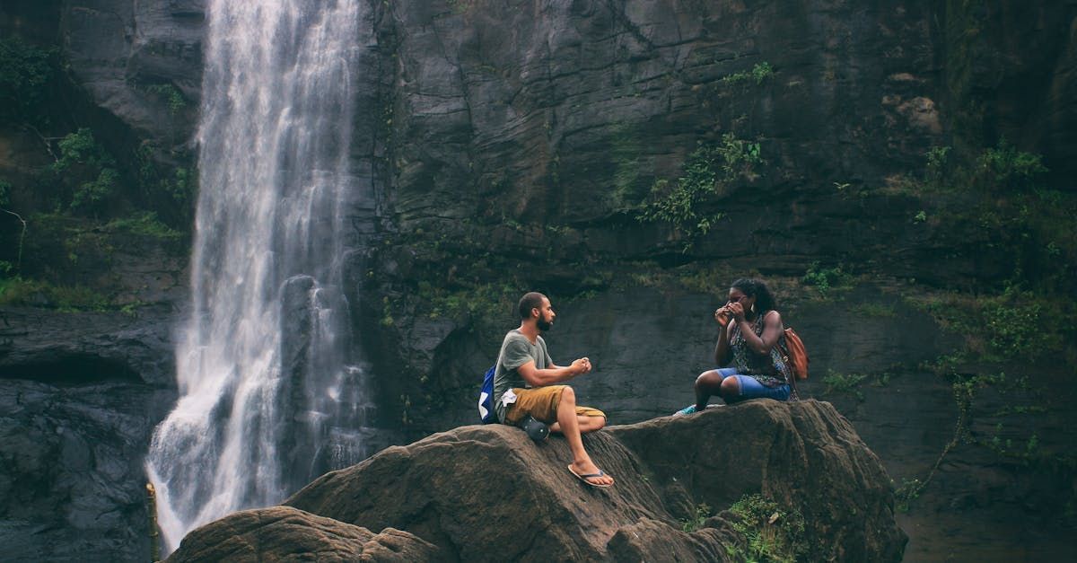 Two people on a rock near a waterfall: one is taking a photo, the other is seated and facing the photographer.
