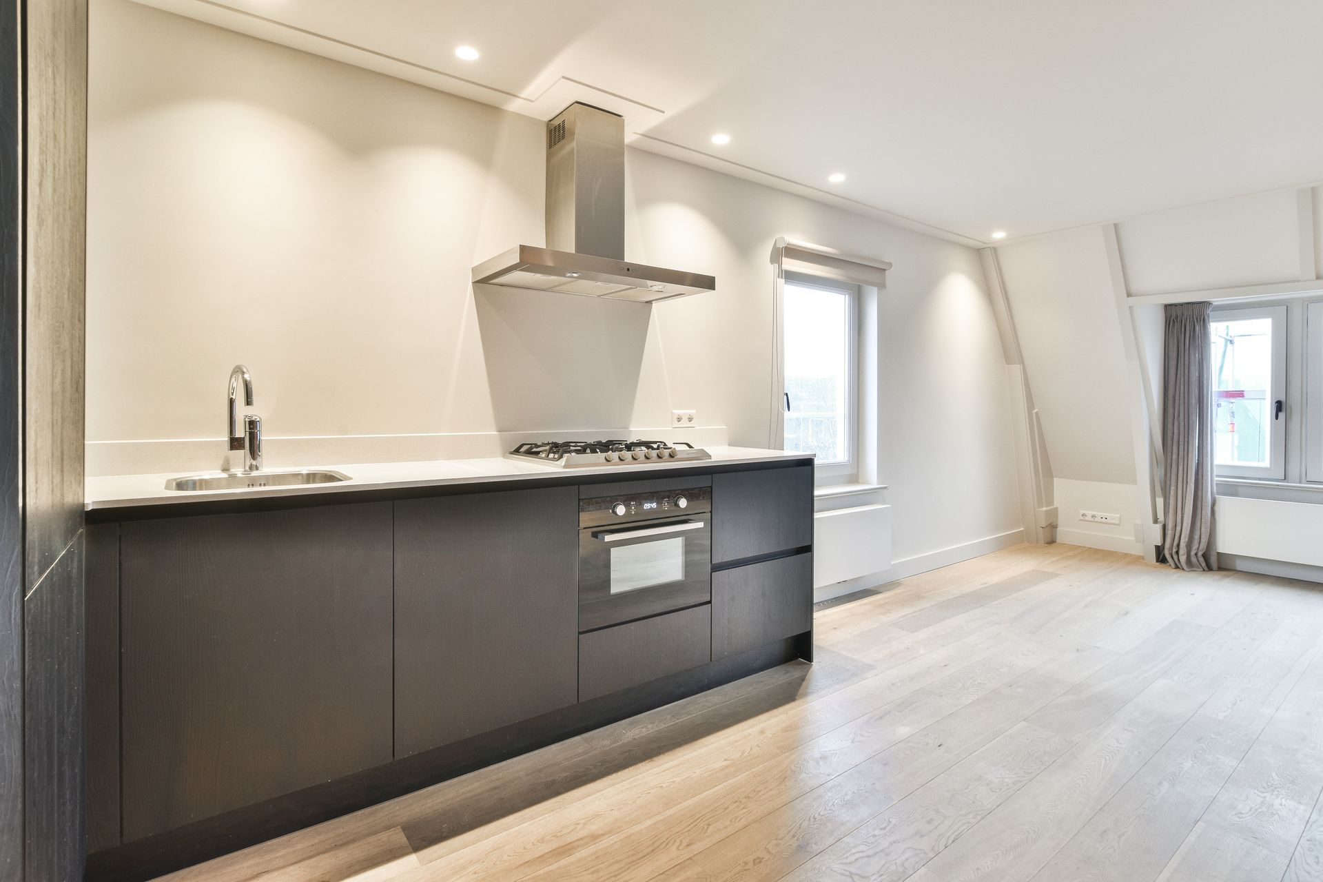 Modern white kitchen with dark cabinets, stainless range hood, and bright open living area
