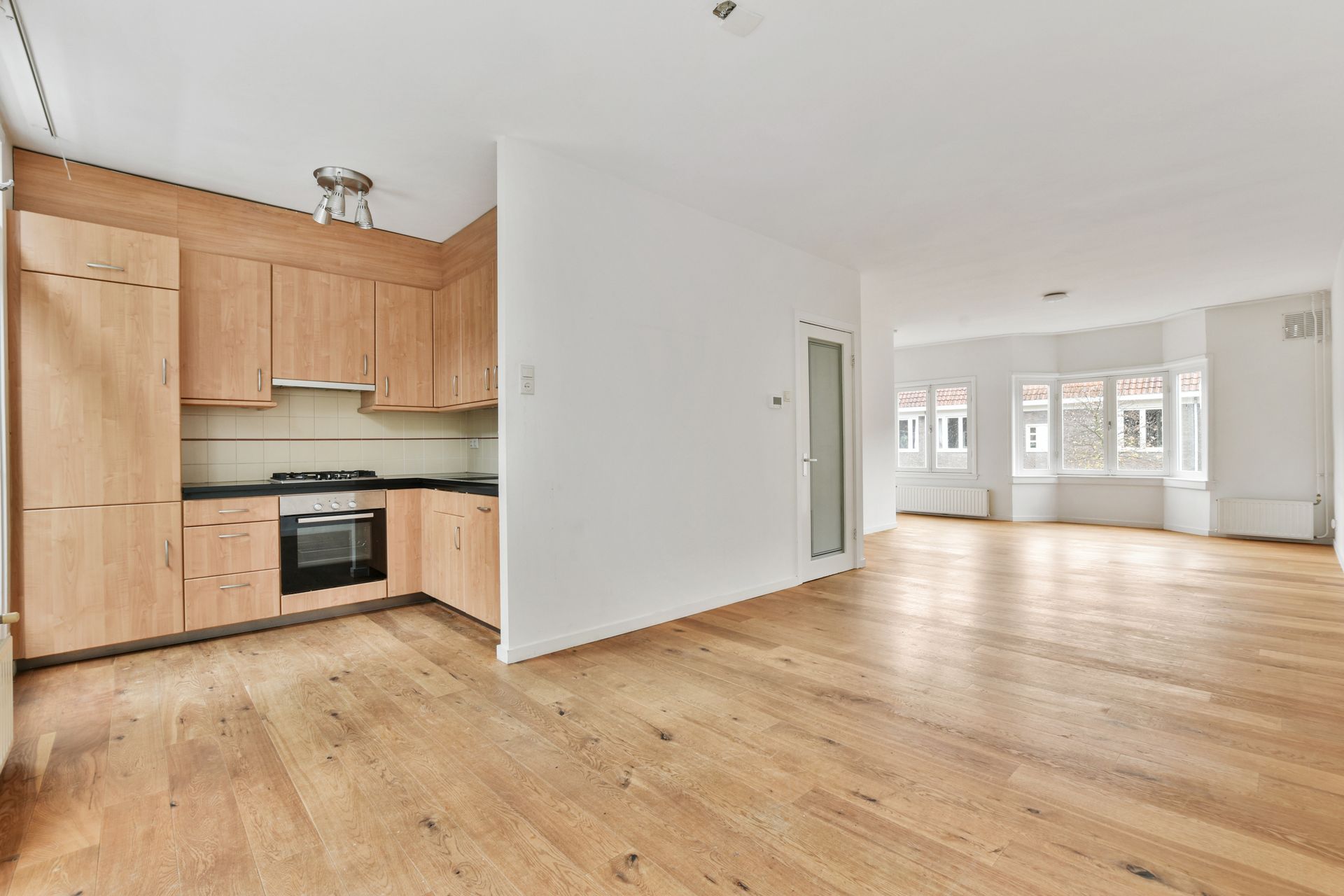 Bright open apartment with wood floors, white walls, and a small kitchen with light wood cabinets.