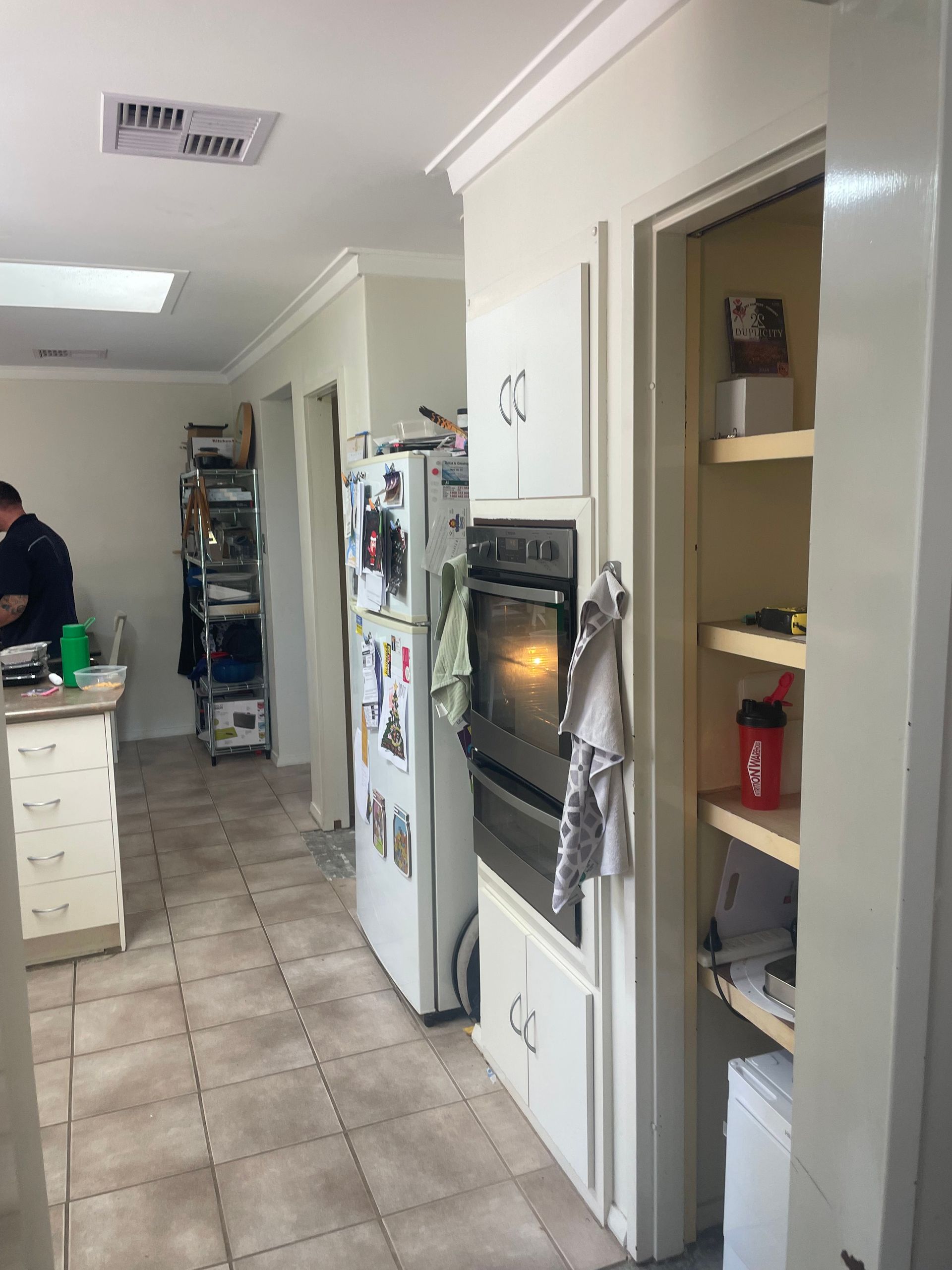 Kitchen hallway with white cabinets, built-in oven, tiled floor, and open pantry shelves