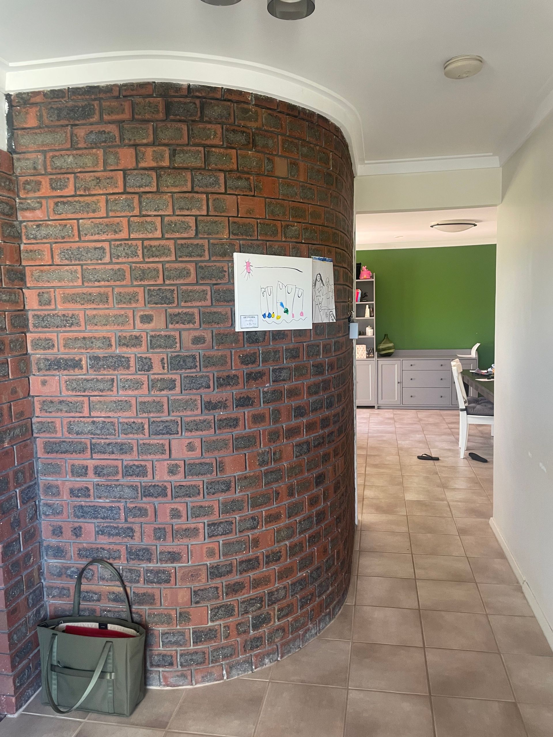Curved brick wall in a tiled interior hallway leading to a kitchen with green walls.