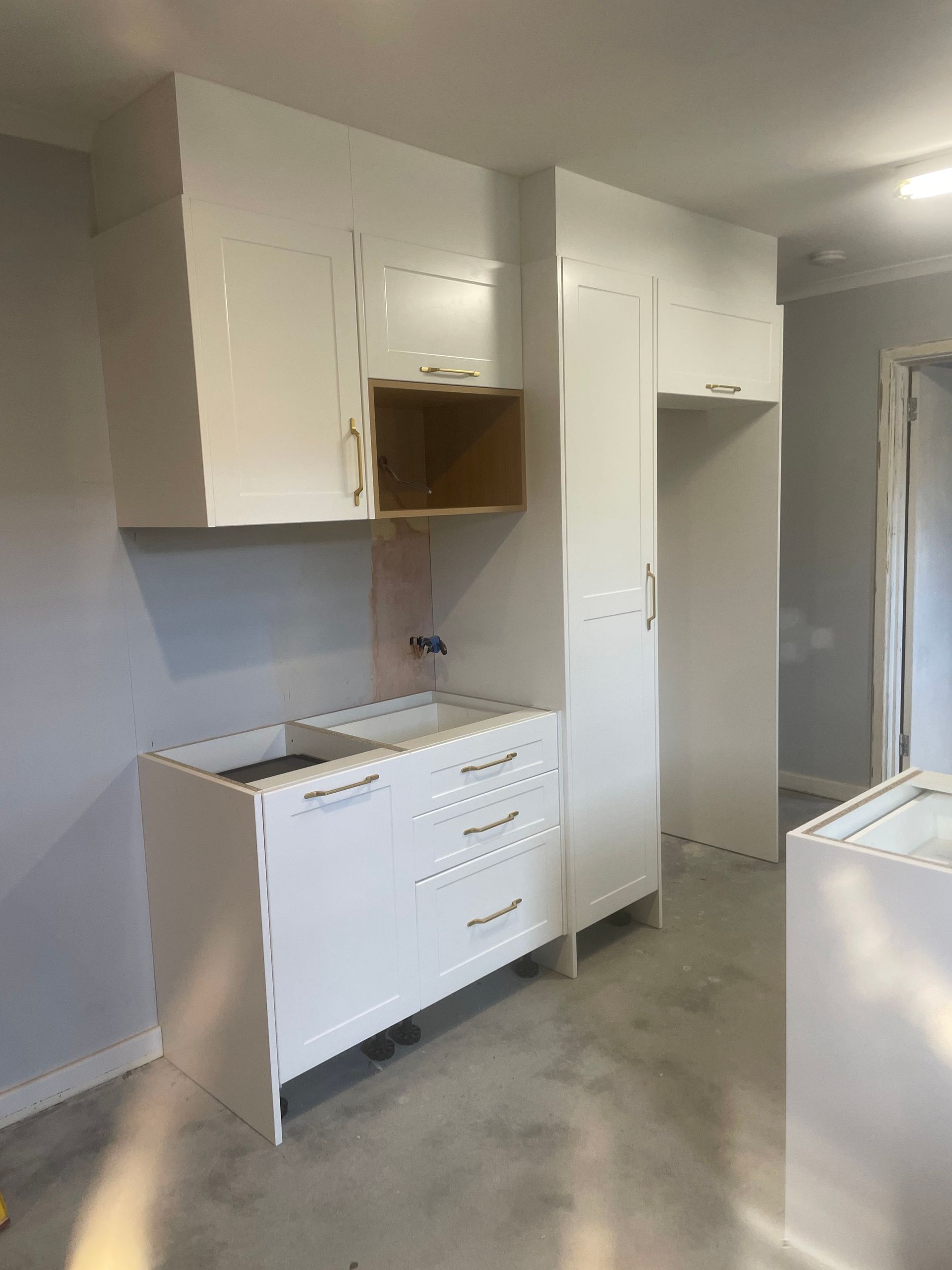 Empty kitchen with white cabinets, sink, and drawers in a partially renovated room