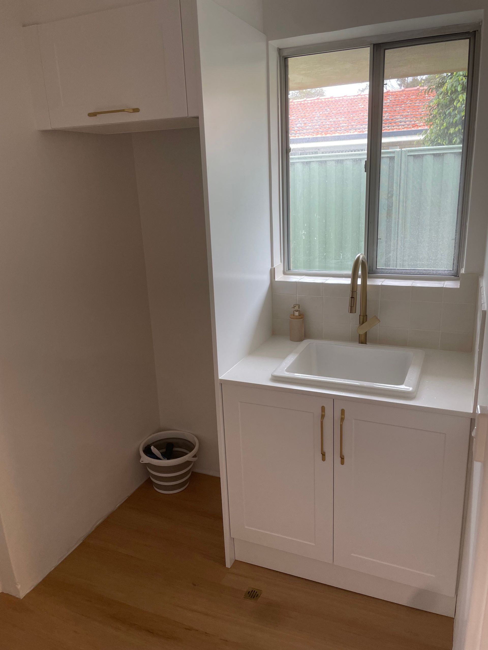 Small kitchen nook with white sink cabinet, window, and light wood floor beside an open closet area
