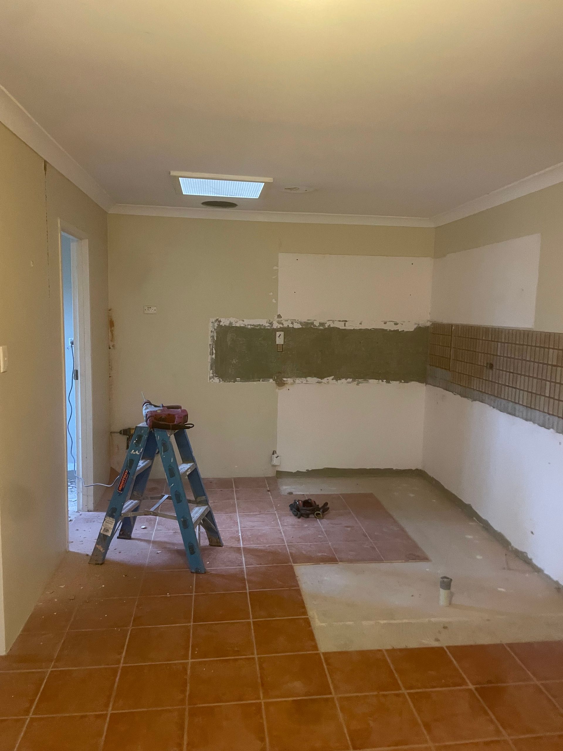 Partially tiled room under renovation with ladder, patchy walls, and tools on the floor