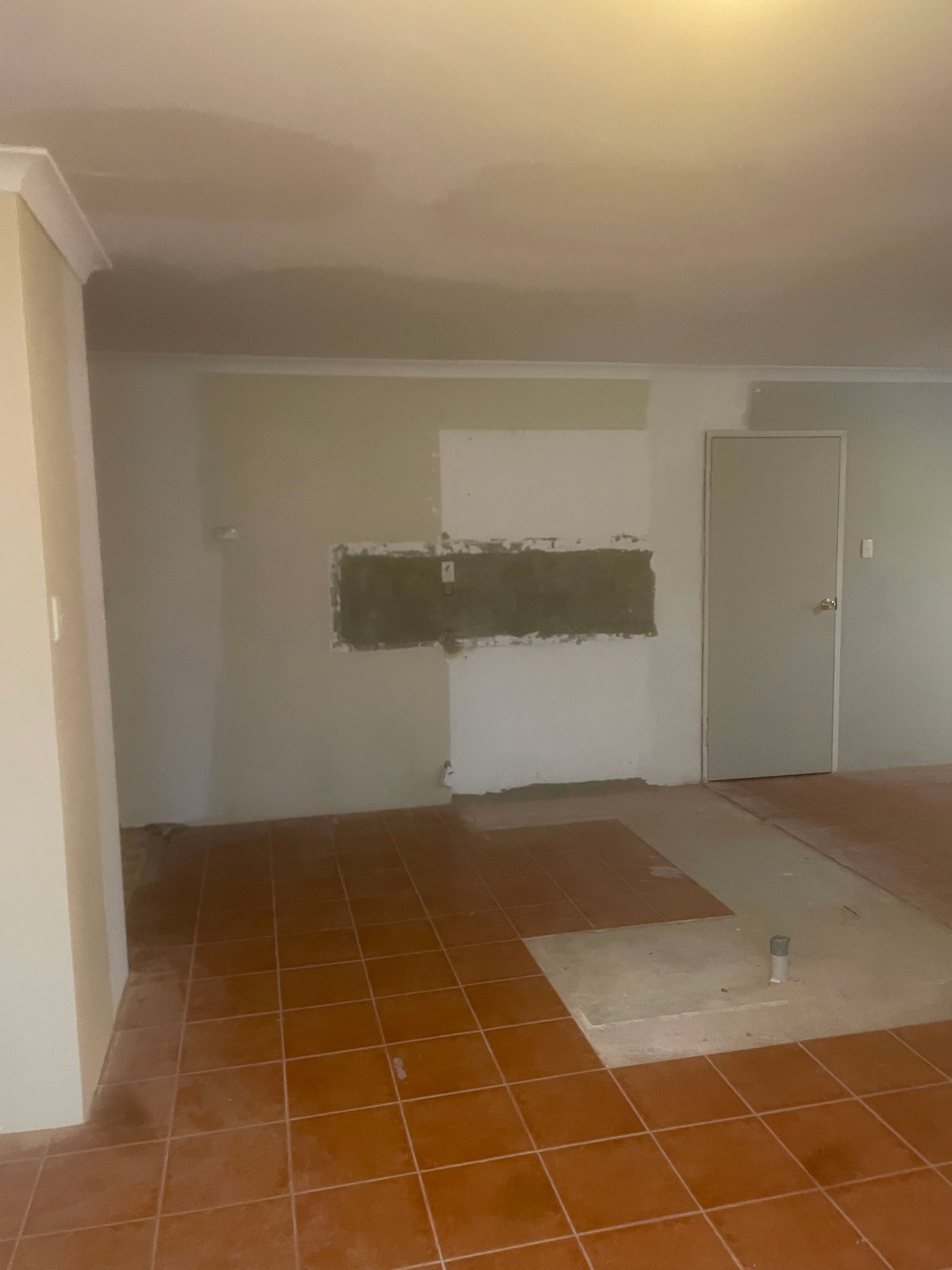 Empty room with terracotta tile floor, pale walls, and a small window or vent on the back wall.
