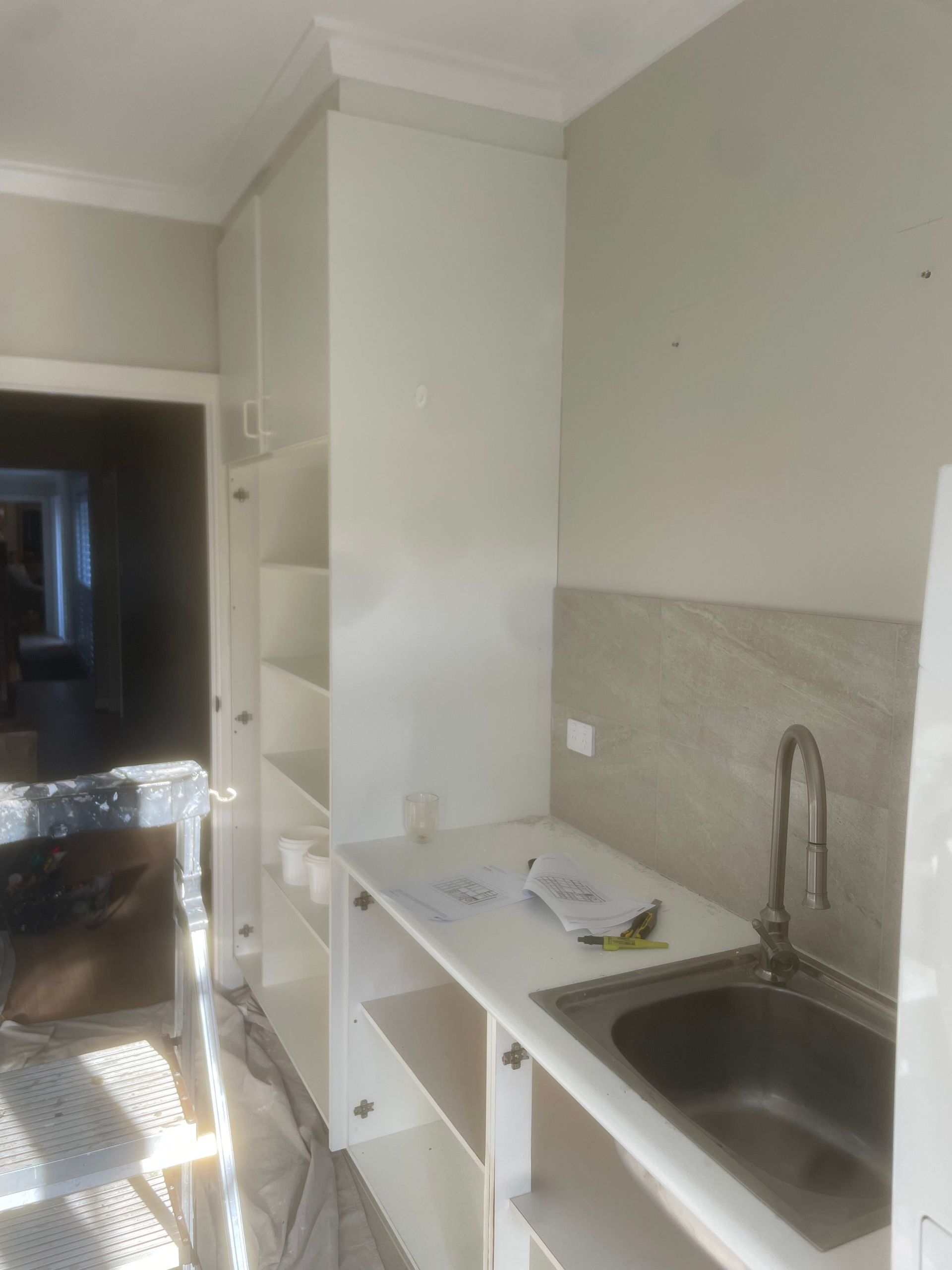 Small kitchen with white cabinets, stainless sink, countertop, and open doorway to a dark hall.
