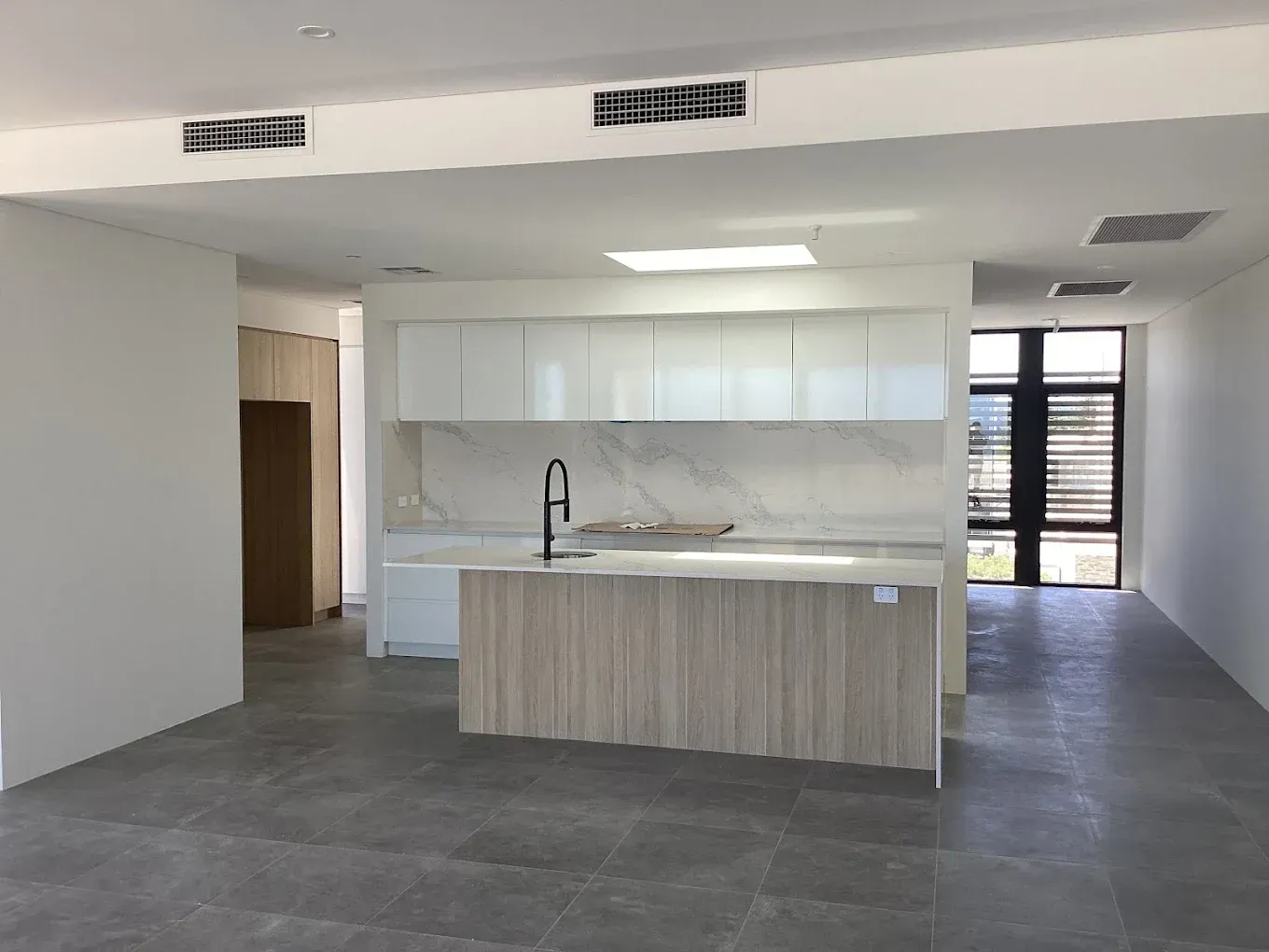 Modern kitchen with white cabinets, island sink, gray tile floor, and sliding glass doors to a patio.