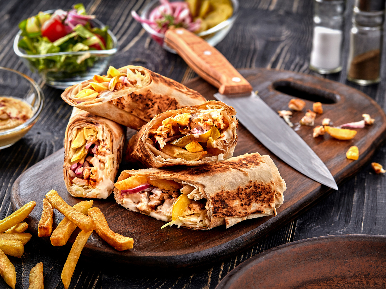 A wooden cutting board topped with shawarma and french fries.