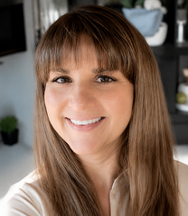 Smiling person with brown hair and bangs sitting inside a car.