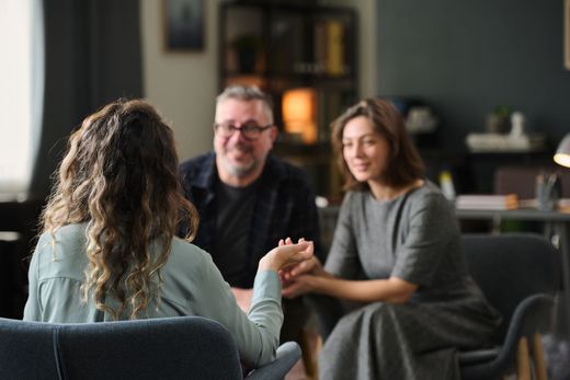 Three people in a cozy lounge, seated in conversation with a coffee table nearby.