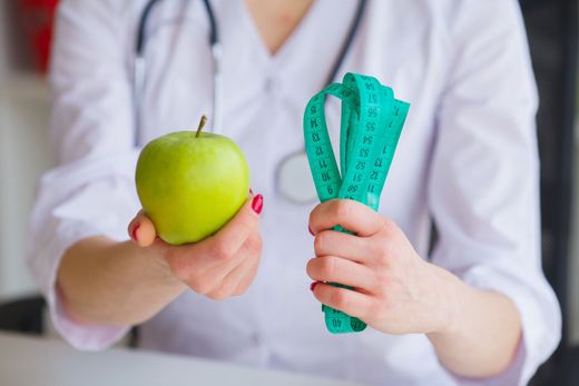 Person holding a green apple and a teal measuring tape, suggesting healthy eating and weight loss.