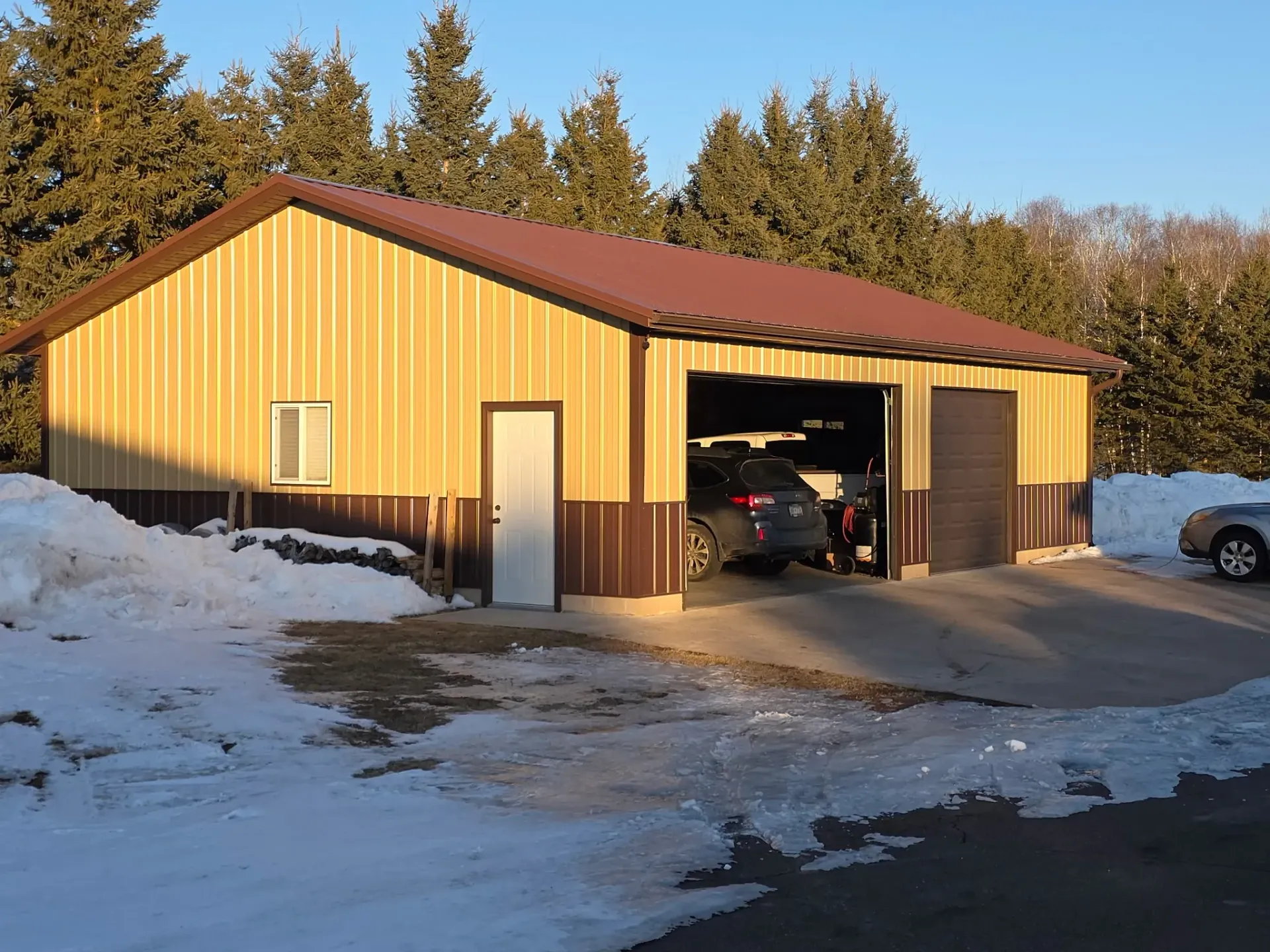 Yellow metal garage with open doors in a snowy yard at sunset