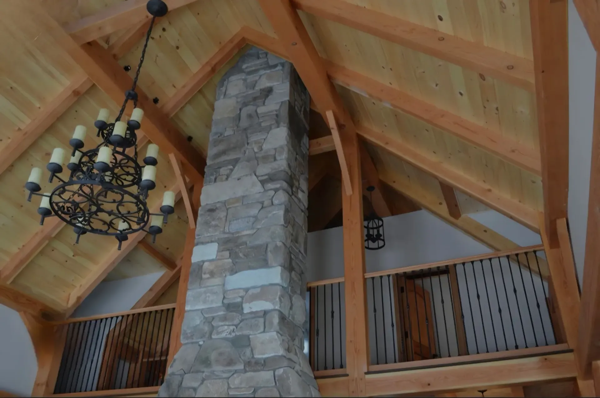 Rustic lodge interior with a tall stone chimney, wood beams, and a chandelier beneath a vaulted ceiling