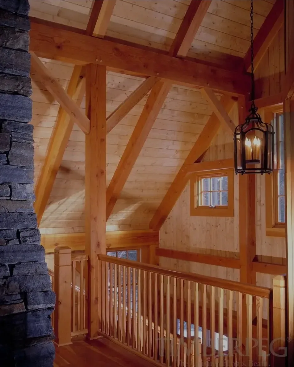 Wooden loft interior with exposed beams, railing, and hanging lantern beside a stone wall.
