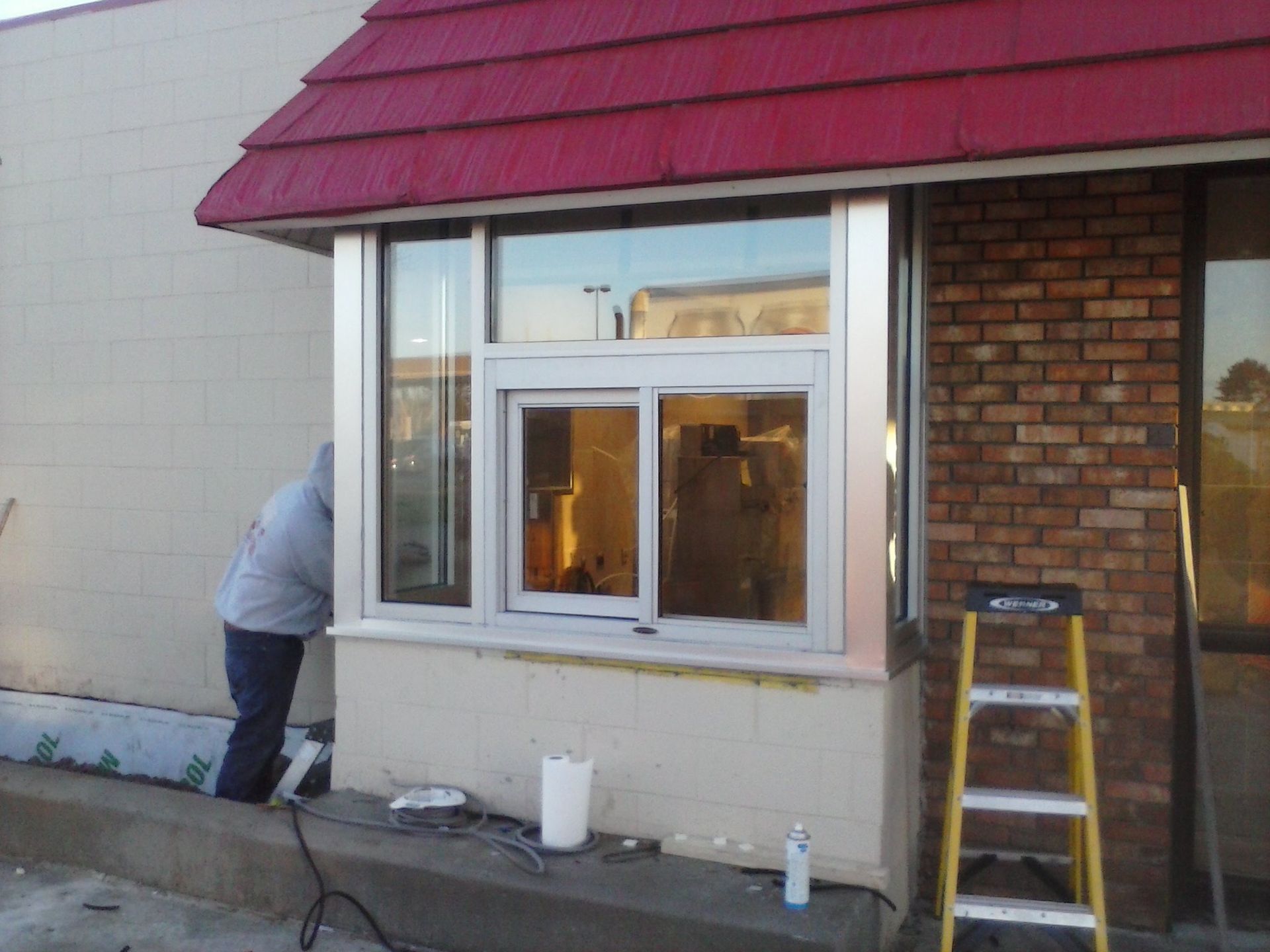 Worker painting exterior wall of a building beside a window and ladder