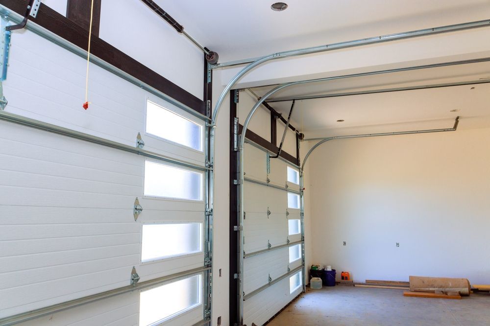 Empty garage interior with open white sectional doors and a few tools on the floor