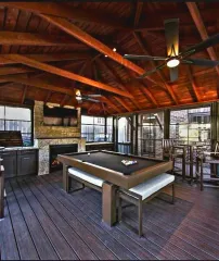Rustic covered patio with a pool table, wooden ceiling beams, and bar seating overlooking greenery