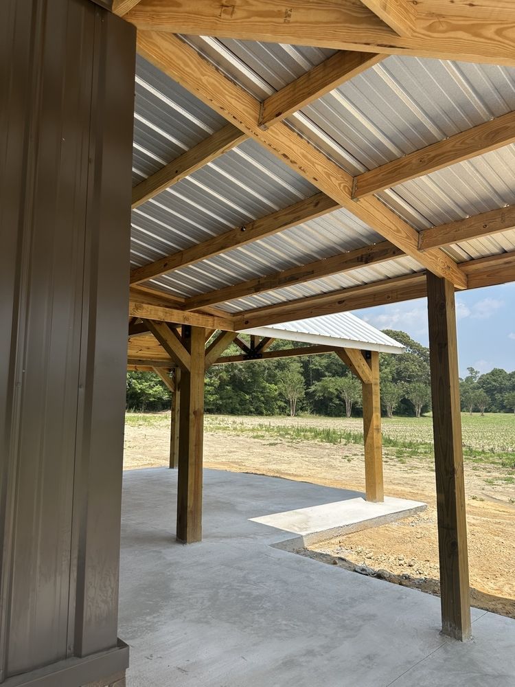 Covered concrete patio with wooden posts and corrugated metal roof, overlooking a dry grassy field.