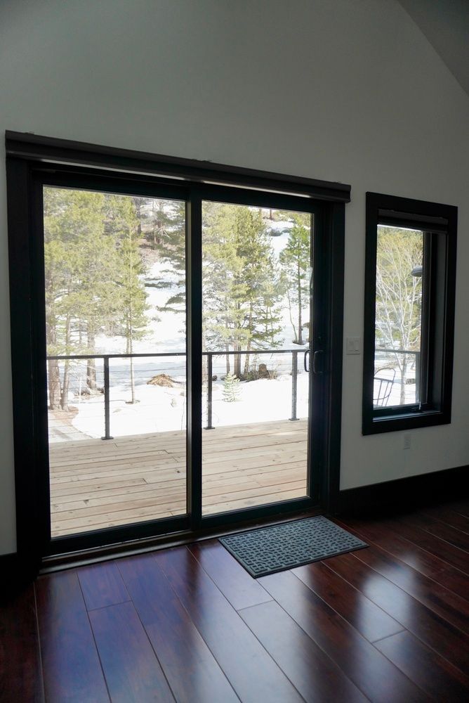 Sliding glass doors and a narrow window opening to a snowy deck and trees, with dark wood floors inside