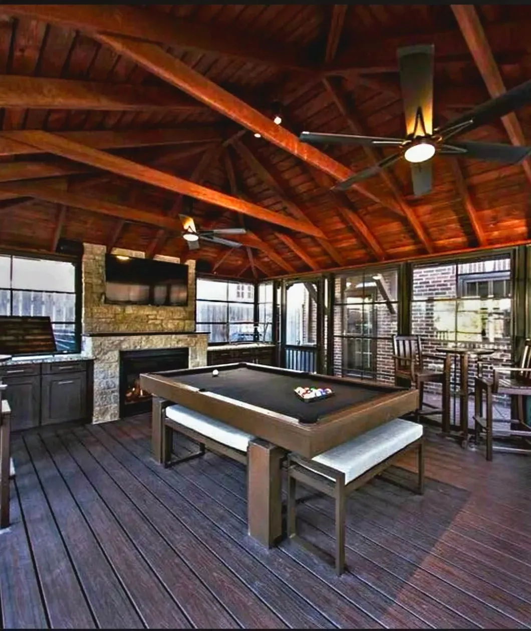 Covered outdoor game room with pool table, bar stools, and wood-paneled vaulted ceiling