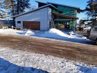 Snowy driveway beside a metal-sided house with a garage, green upper level, and parked vehicle.
