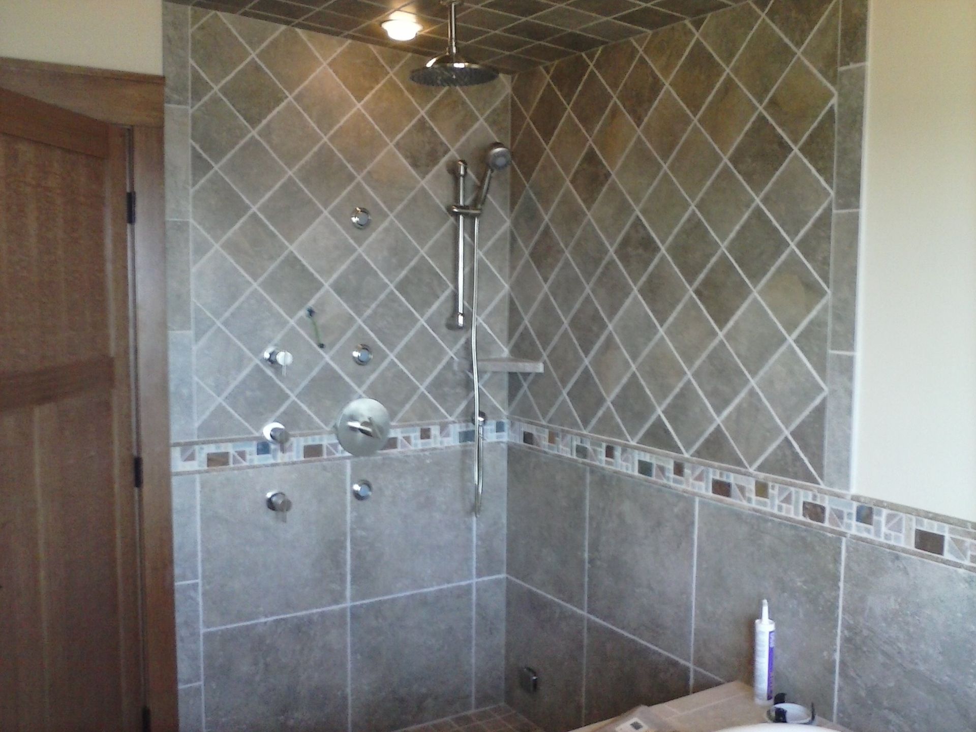 Bathroom shower with gray tiled walls, glass doors, and a handheld showerhead.