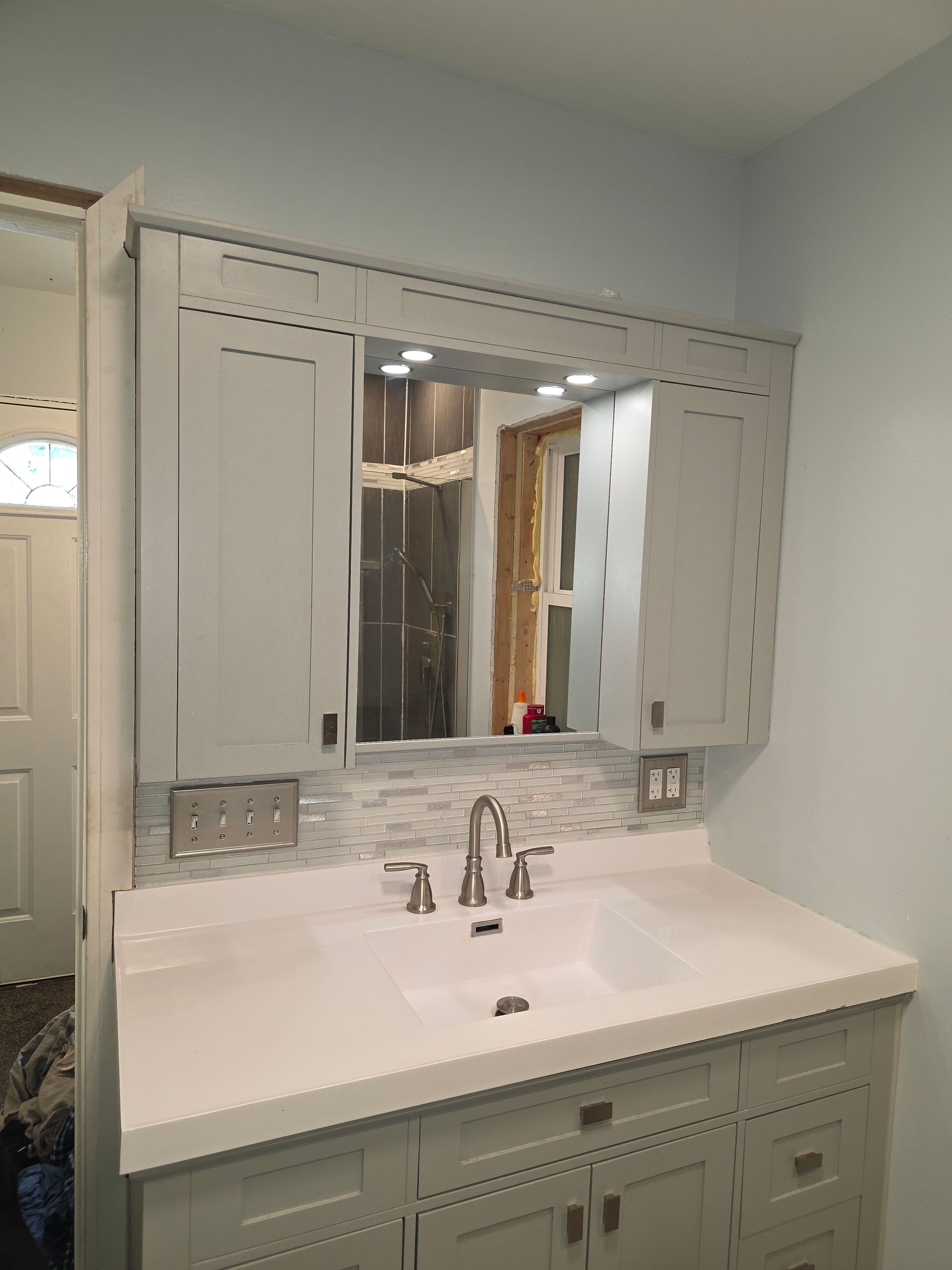White bathroom vanity with sink, mirrored cabinet, and marble-style backsplash next to a doorway.