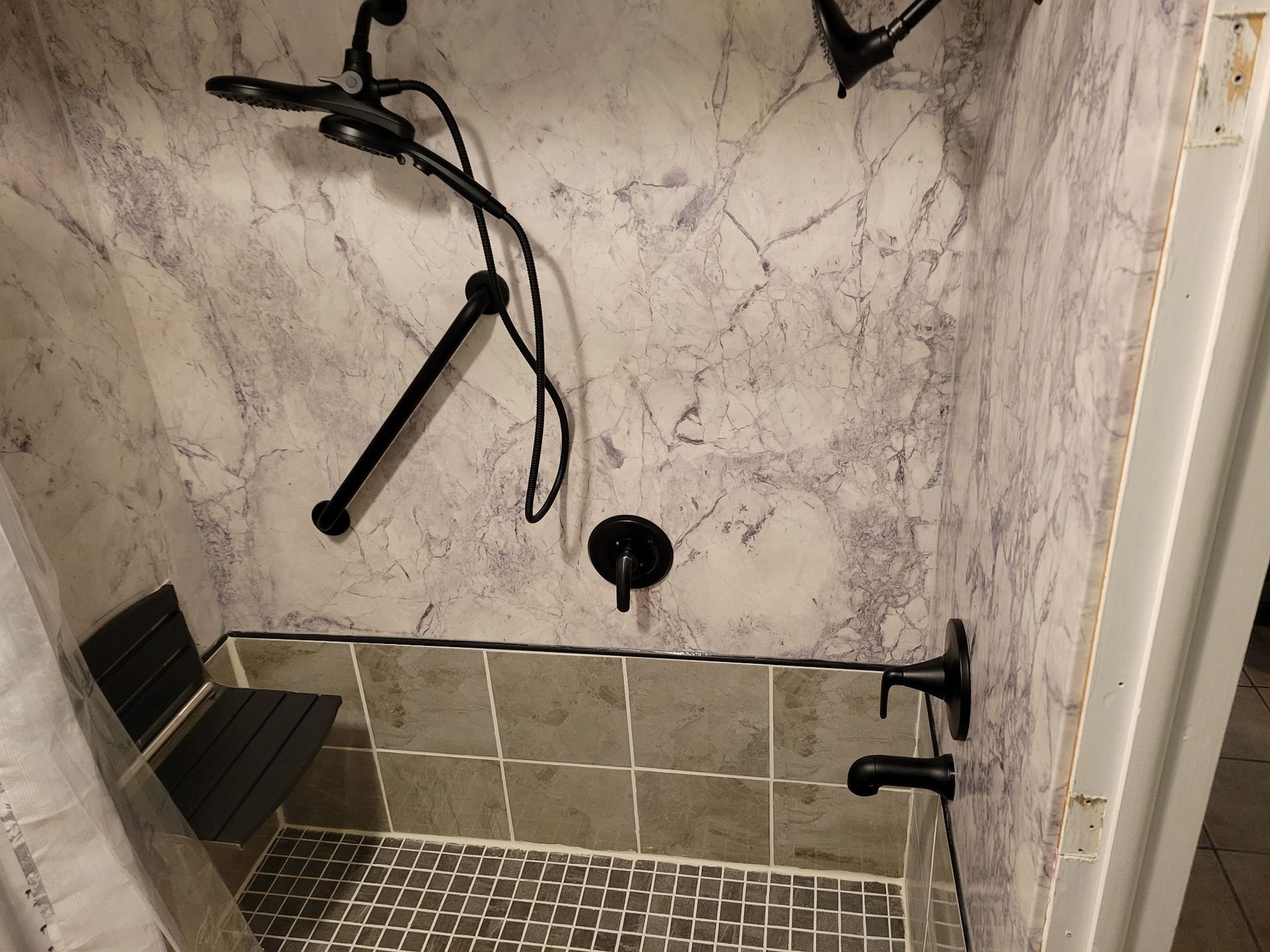 Walk-in shower with beige tile, black grab bars, a shower bench, and adjustable shower fixtures.